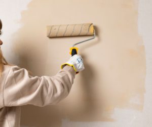 Woman painting newly primed plaster wall with a roller