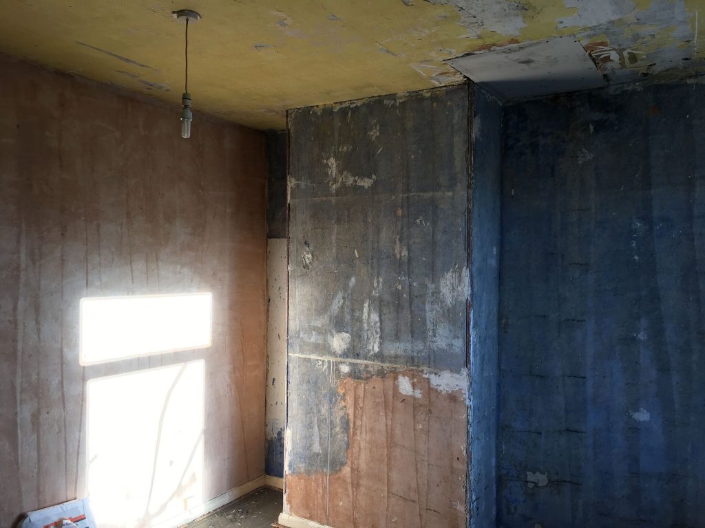 Room with damaged and uneven walls and ceiling before skimming