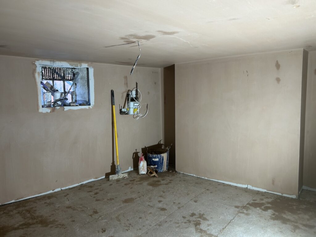 Newly plastered basement room showing smooth wall finishes around a window and adjoining walls