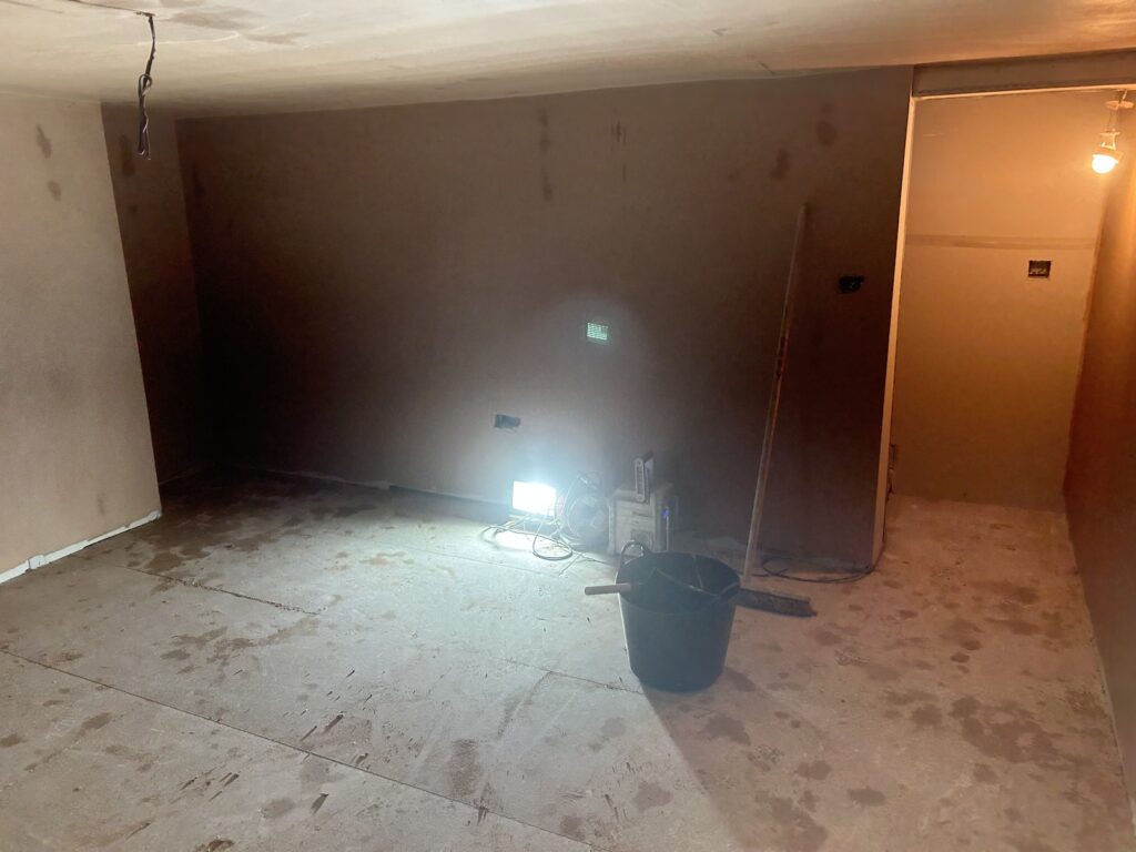 Newly plastered basement walls with a smooth plaster finish and unfinished floor during renovation work